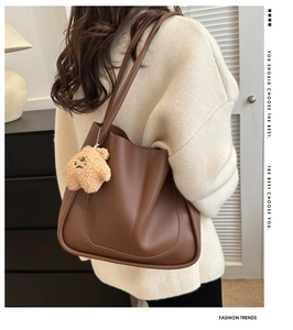 Detail of dark brown leather tote bag with U-shaped stitching and plush bear charm