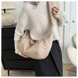 Detail of a large beige nylon crescent bag worn over a cream cable knit sweater