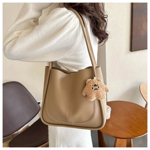 Detail of khaki tote bag with plush bear charm and minimalist stitching in a cafe setting