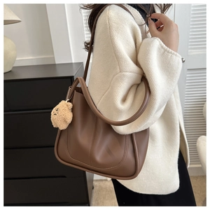 Detail of a brown faux leather tote bag with thick stitching and a cute bear charm