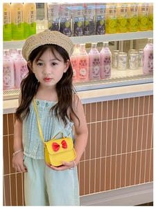 Sac à bandoulière jaune pour fille avec nœud rouge, porté par un enfant mannequin