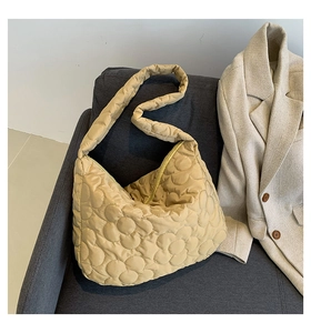 Beigefarbene gesteppte Puffer-Tasche mit Blumenmuster auf einem grauen Sofa im Lifestyle-Look