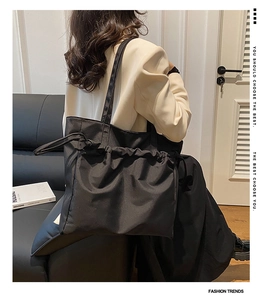 Detalle de un bolso tote grande de nailon negro con diseño plisado y correa larga al hombro