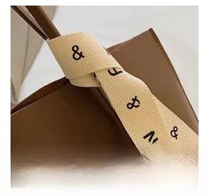 Detail of a dark brown leather tote handle with a knotted beige fabric scarf accent