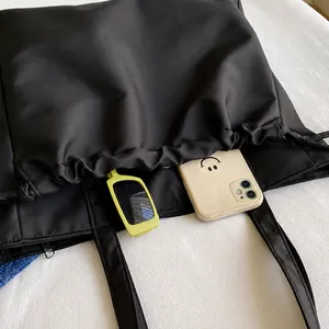 Detail view of large black tote bag side drawstring pocket with phone and sunglasses