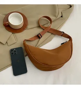 Detail of a brown nylon half-moon crossbody bag with adjustable strap in casual setting