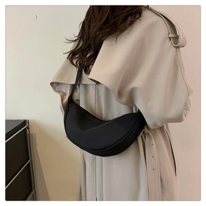 Model wearing a black nylon crescent crossbody bag with a tan trench coat view