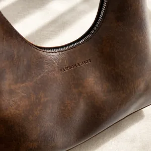 Détail de la texture cuir vintage marron foncé et logo FASHION & BAGS embossé sur le sac