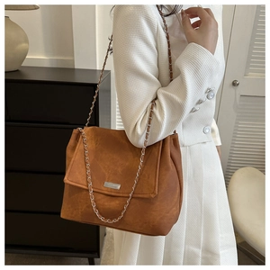 Détail d'un sac cabas en daim marron avec bandoulière chaîne argentée et boucle métal