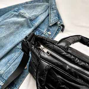 Detail of a smooth silver metal zipper on a glossy black puffer shoulder bag with wide strap
