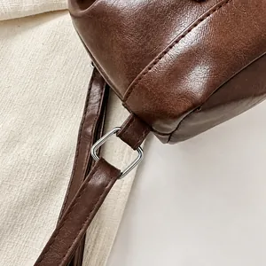 Detail of square silver metal buckle and stitching on dark brown leather shoulder bag