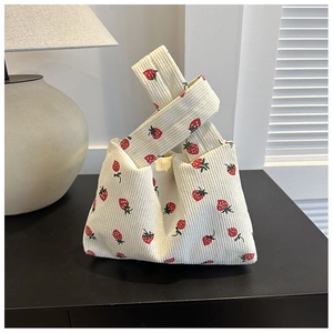 Detail of soft beige corduroy fabric with red strawberry print on knotted handbag
