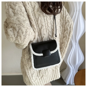 Detail van zwarte leren crossbodytas met witte bontrand en een getextureerde gebreide trui