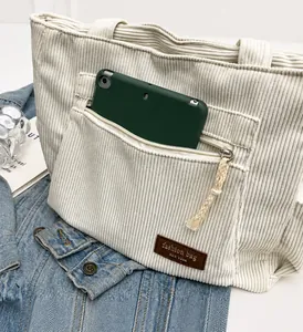 Detail of white corduroy tote bag showing front zipper pocket with a green tablet inside