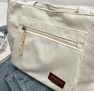 Close-up of off-white corduroy tote bag showing striped texture and zipper pocket details