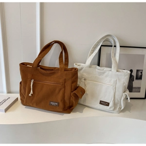 Detail of corduroy tote bags showing front zipper pocket and side pockets in brown and beige