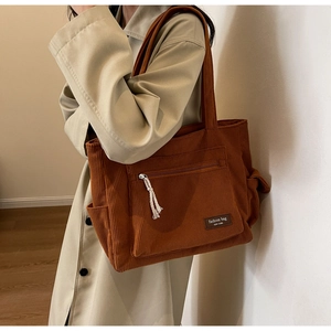 Detail of brown corduroy tote bag showing front zipper pocket and decorative white tassel