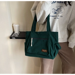Detail of dark green corduroy tote bag with side pocket and fashion label on shoulder