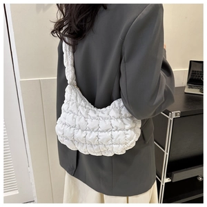Detailed view of a white quilted puffer cloud bag worn on a shoulder over a grey blazer