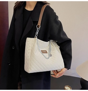 Détail du sac fourre-tout matelassé avec chaîne argentée et patch cuir sur tissu blanc cassé