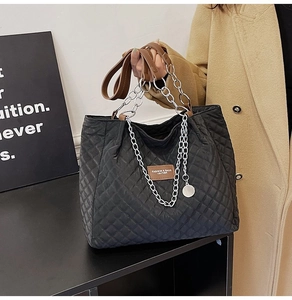 Détail d'un sac cabas noir matelassé avec bandoulière en cuir brun et chaîne argent