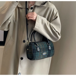 Detail einer karierten Boston Bag aus grünem Wollstoff mit schwarzen Ledergriffen