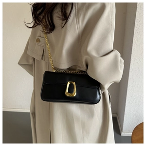Detail einer schwarzen Kettentasche mit goldener Schließe auf beige Trenchcoat