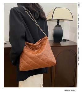 Brown quilted tote bag with gold chain strap shown from a side view on a model