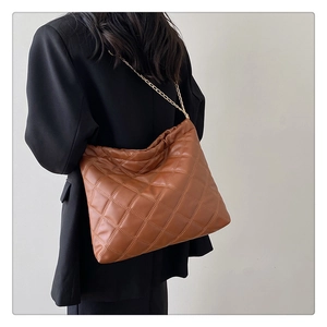 Detailed view of brown quilted leather bucket bag with gold chain strap on model