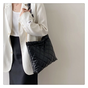 Close-up of black quilted leather bucket bag with gold chain strap on a model