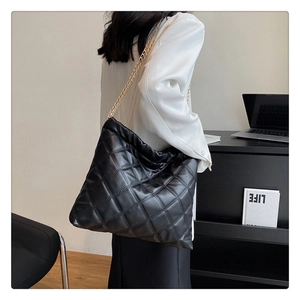 Detail of black quilted tote bag with gold chain strap in a professional office setting