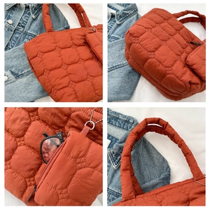 Detail of orange quilted tote bag showing padded texture and detachable mini pouch