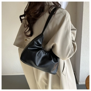 Rear view of a model wearing a chic black soft leather shoulder bag with a trench coat