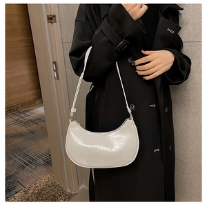 Close-up of minimalist cream crescent shoulder bag worn with a black trench coat