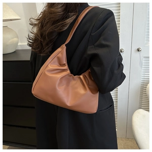 Detail of caramel pleated crescent bag showing leather texture and underarm carry style