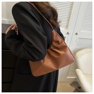 Close-up of caramel pleated PU leather crescent bag with thin shoulder strap on a chair