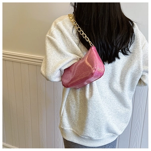 Close-up of pink glitter underarm bag with chunky gold chain strap worn by model