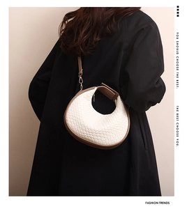 Detail of white woven leather crescent bag with brown handles on black coat