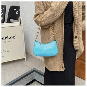Detail of blue glitter baguette bag with chunky gold chain strap worn by a model