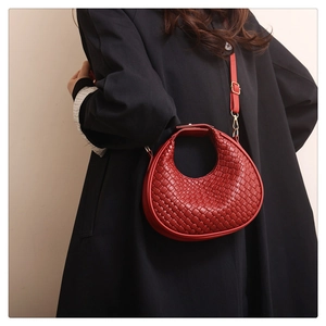 Detail of red woven crescent handbag with adjustable strap worn on black oversize coat