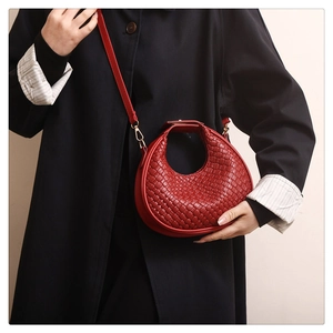 Vue détaillée d'un sac demi-lune tressé rouge porté en bandoulière sur un manteau sombre