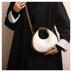 Detail of cream woven crescent handbag with brown leather handle and gold hardware