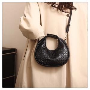 Gros plan du sac demi-lune tressé noir avec motif en point de croix sur un trench-coat