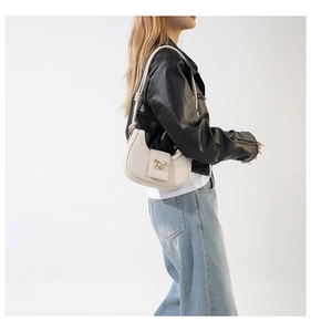 Detail of a creamy white half-moon shoulder bag featuring a gold butterfly buckle accent