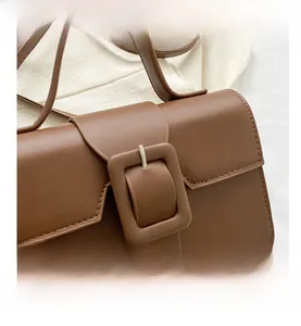 Detail of a brown leather shoulder bag featuring a large square buckle and retro flap design