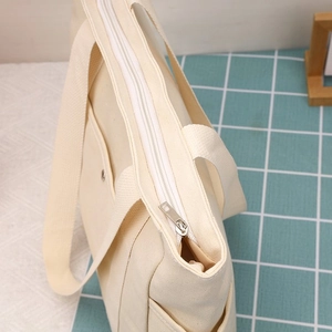 Dettaglio borsa tote in tela crema con chiusura a zip metallica e tasca laterale