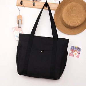 Dettaglio di una borsa tote in tela nera con tasche laterali appesa a un appendiabiti