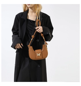 Close-up of brown crescent bag with gold butterfly accent and knotted strap detail