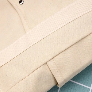 Dettaglio ravvicinato della borsa in tela beige con cuciture e bottone a pressione in metallo