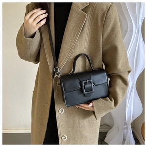 Close-up of black retro leather handbag with matte square buckle and shoulder strap